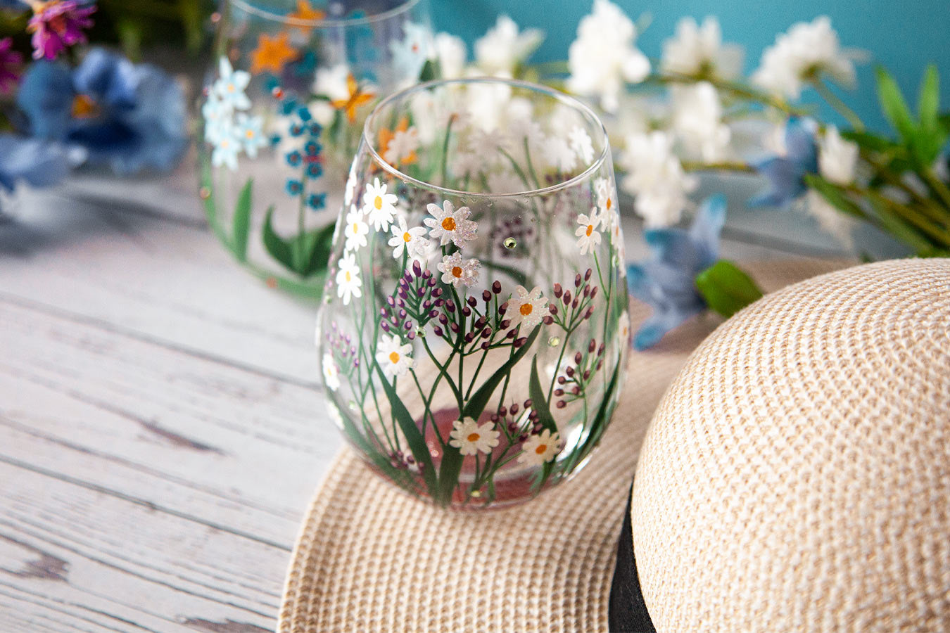 Stemless wine glass with floral design on a wooden table with flowers in the background