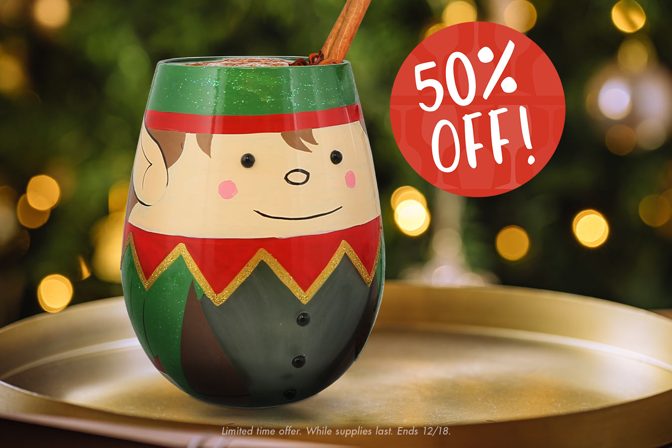 Elf-themed wine glass with a cinnamon stick on a gold tray, Christmas tree in the background, and '50% Off!' sign.